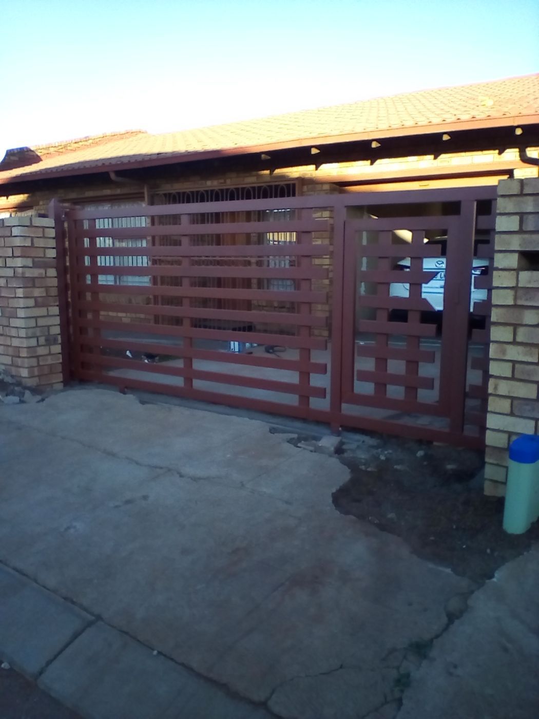 A wide maroon steel driveway gate between brick pillars