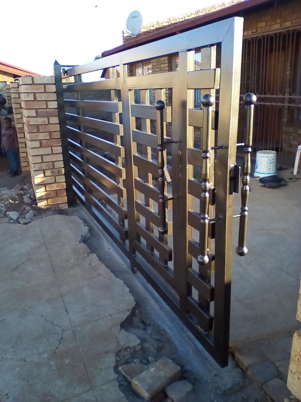 A dark steel security gate with horizontal slats installed between brick pillars